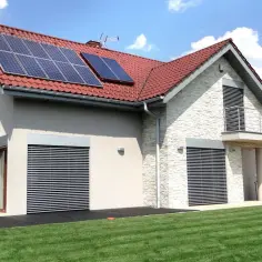 Nowoczesny dom z panelami solarnymi na dachu, kamienną elewacją i zielonym trawnikiem.