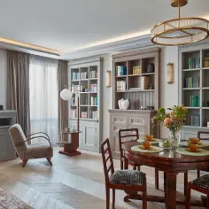 Elegancki salon w stylu klasycznym. Okrągły stół z krzesłami, regały z książkami, fotel i obraz tworzą przytulną atmosferę.