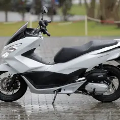 Biały skuter Honda PCX na mokrym bruku. Idealny na pierwsze samodzielne przejażdżki, bo od ilu lat można jeździć 50?