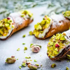 Chrupiące rurki wypełnione kremem i posypane pistacjami – pyszne cannoli na kamiennym blacie.