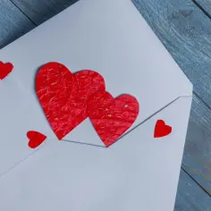 Biała koperta z czerwonymi serduszkami, symbolizująca początkowe, intensywne oznaki miłości, które mogą być częścią zjawiska znanego jako love bombing objawy.
