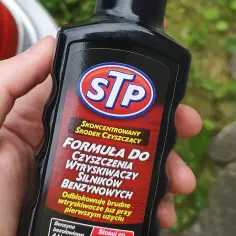 Dłoń trzyma butelkę STP z napisem "Formuła do czyszczenia wtryskiwaczy benzynowych".