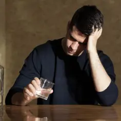 Mężczyzna z ręką na głowie, obok butelki i szklanki. Czy to walka z depresją i ssri a alkohol?
