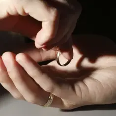 Dwie dłonie trzymają złotą obrączkę, zastanawiając się, gdzie sprzedać obrączkę. Jedna dłoń ma już inną obrączkę.