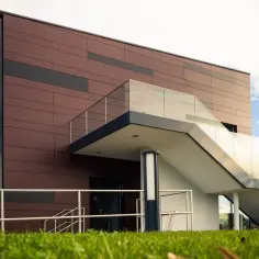 Nowoczesna elewacja z płyt HPL w odcieniach brązu i czerni, z przeszklonymi balustradami schodów zewnętrznych.