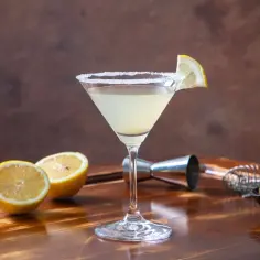 Koktajl Martini Bianco w kieliszku z solą na brzegu, udekorowany plasterkiem cytryny, obok cytryny i oliwki.