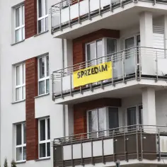 Nowy budynek mieszkalny z żółtym banerem "SPRZEDAM" na balkonie.