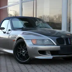 Srebrny kabriolet BMW E37 z czarną maską i felgami BBS, zaparkowany przed budynkiem z dużymi oknami.