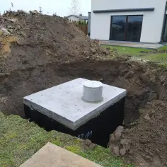 Zbiornik na wodę opadową w wykopie. Budowa domu w toku, ziemia usypana obok.