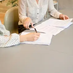Dwie kobiety przy stole omawiają umowę przedwstępną sprzedaży nieruchomości. Jedna pisze notatki.