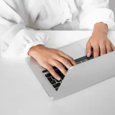 Osoba w białej bluzce pisze na laptopie, przygotowując zaświadczenie o niezaleganiu.