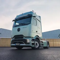 Nowy Mercedes Actros MP4 w kolorze miętowym, zaparkowany przed halami magazynowymi.