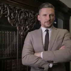 Mężczyzna w garniturze stoi przed regałem z książkami.