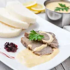 Pokrojony schab z sosem, knedlami, konfiturą i cytryną.
