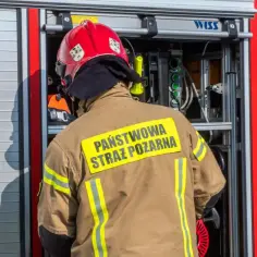 Strażak w mundurze Państwowej Straży Pożarnej przy wozie bojowym. Zastanawiasz się, ile zarabia strażak na start?