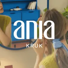 Kobieta w lustrze poprawia kolczyk, a na jej nadgarstku widać delikatną bransoletkę. Logo Ania Kruk.