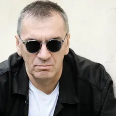 Maciej Pasikowski w okularach przeciwsłonecznych, oparty o ścianę. Może opowiadać historie o swoich dzieciach.