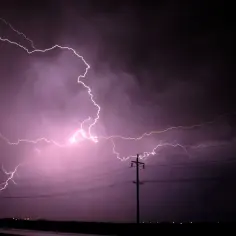 Potężne wyładowanie elektryczne rozświetla fioletowe chmury. Widać słupy energetyczne, jakby symbolizowały przepływ mocy, gdzie P = U * I.