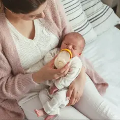 Mama karmi noworodka butelką, ucząc się jak karmić noworodka butelką. Delikatny dotyk i miłość w tym ważnym momencie.