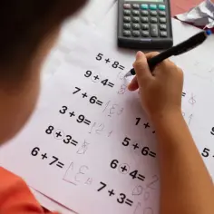 Dziecko rozwiązuje zadania matematyczne, które mogą być częścią dyskalkulia testu. Widać trudności z zapisem wyników.