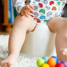 Dziecko siedzi na nocniku, bawiąc się kolorową zabawką. To ważny krok, jak nauczyć dziecko korzystać z nocnika.