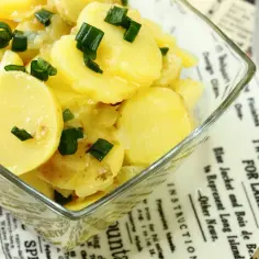 Oryginalna kartoffelsalat z ziemniaków, cebuli i szczypiorku w szklanej misce.