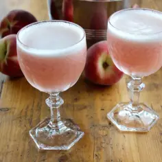 Dwa różowe drinki z pianką, obok brzoskwiń, na drewnianym stole. To jest właśnie co to znaczy drink – orzeźwienie i smak.
