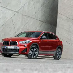 Czerwone BMW X2 2025 z nowoczesnym designem, zaparkowane przy betonowej ścianie.