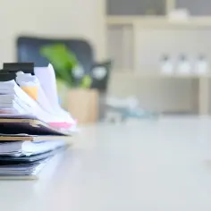 Stos dokumentów, w tym dokumenty regulujące pracę przedszkola, czeka na biurku. Obok leży długopis.
