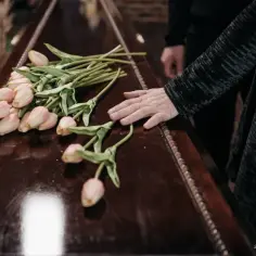Dłoń na trumnie z tulipanami. Zastanawiasz się, ile kosztuje kremacja zwłok w Niemczech?
