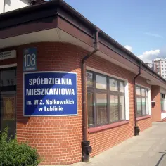 Budynek spółdzielni mieszkaniowej z niebieskim szyldem i ceglaną elewacją.
