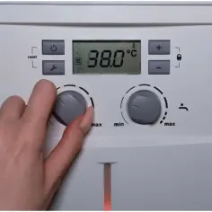 Dłoń reguluje pokrętłem temperaturę na panelu bojlera z cyfrowym wyświetlaczem 38.0°C.