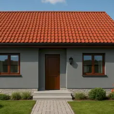 Dom z ceglastym dachem i szarą elewacją, otoczony zielenią.