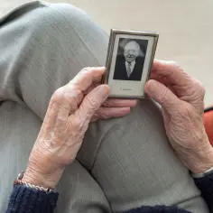 Dłonie starszej osoby trzymają małe zdjęcie z napisem "In memoriam". Czasem zastanawiamy się, ile trwa żałoba.