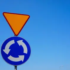 Znak ustąp pierwszeństwa i znak informujący o ruchu okrężnym na tle błękitnego nieba.