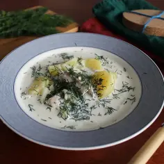 Zupa śledziowa z ziemniakami i koperkiem w talerzu, obok łyżka i pęczek koperku.