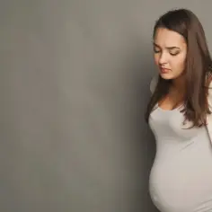 Kobieta w ciąży z bólem pachwin, trzymająca się za plecy.