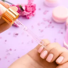 Dłoń z różowymi paznokciami, pipetka z olejkiem do skórek. Zastanawiasz się, jak szybko rosną paznokcie?