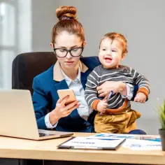 Pracująca mama z dzieckiem na rękach sprawdza telefon. Kto wypłaca macierzyński pracodawca czy ZUS?