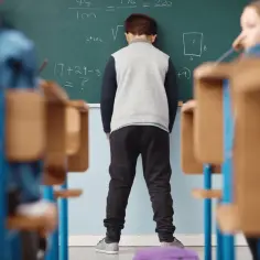 Chłopiec stoi przed tablicą, czując lęk u dzieci przed zadaniem matematycznym. W tle widać innych uczniów.