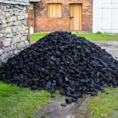 Góra węgla przy kamiennym budynku. Zastanawiasz się, ile kosztuje tona węgla?