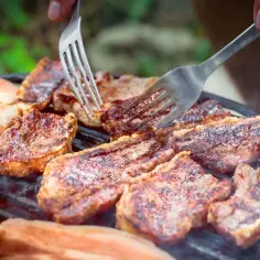 Soczysty boczek na grillu, idealny do marynaty. Dwa widelce obracają kawałki mięsa, które apetycznie skwierczą.