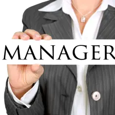 Osoba w garniturze trzyma tabliczkę z napisem "MANAGER". To symbol skutecznego stylu kierowania.