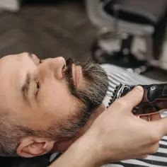 Mężczyzna z siwiejącą brodą jest przycinany trymerem. Czy to golarka Braun czy Philips?