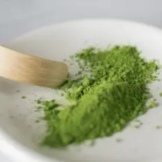 Zielony proszek matcha na białej miseczce z bambusową łopatką.