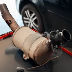 Zużyty filtr DPF na stole warsztatowym, obok koła samochodu.