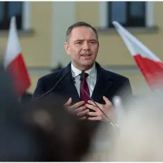 Mężczyzna w garniturze i płaszczu przemawia przy mikrofonach, za nim polskie flagi. Czy zastanawiałeś się, ile zarabia prezydent Polski?