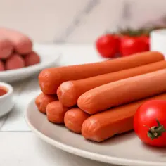 Na talerzu ułożone są apetyczne serdelki, obok pomidorki i sos.