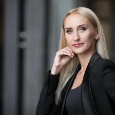 Portret kobiety w czarnej marynarce, z dłonią przy podbródku.