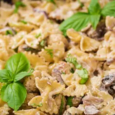 Szybkie dania jednogarnkowe: makaron farfalle w kremowym sosie z kurczakiem i pieczarkami, udekorowany bazylią.